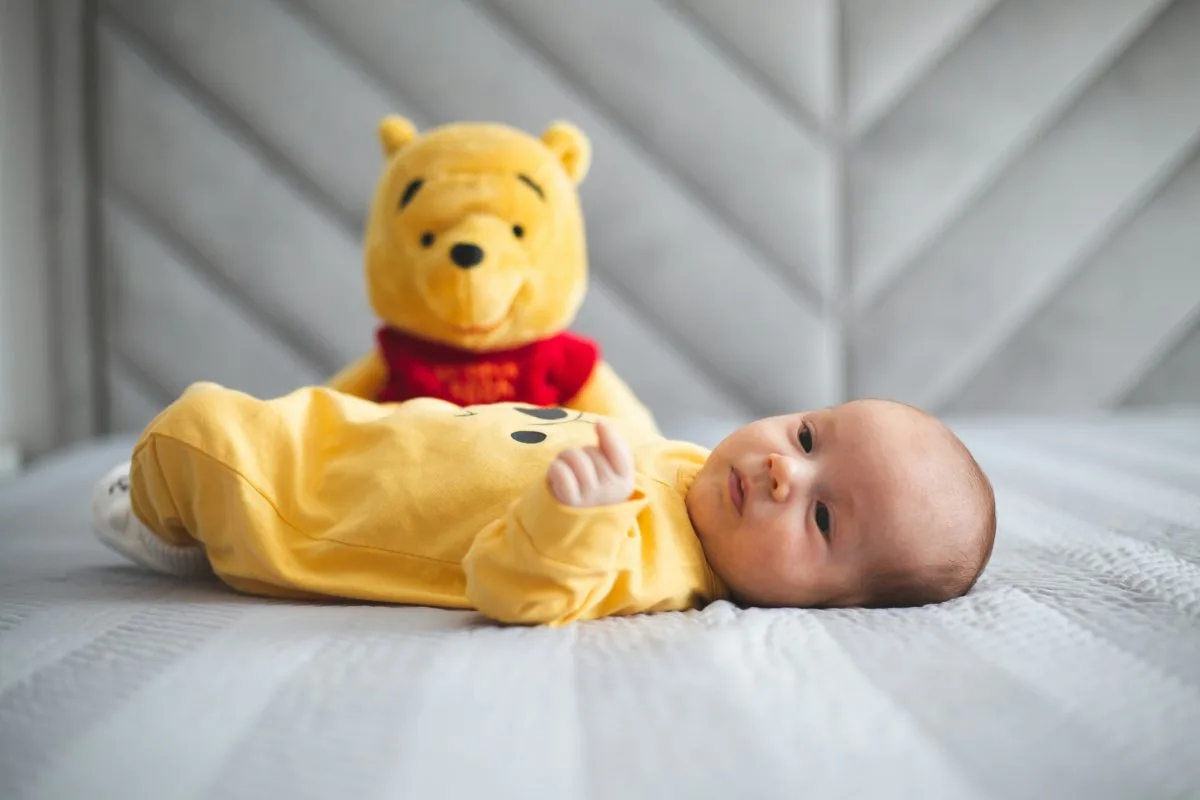 Bébé allongé sur le dos à côté d'une peluche Winnie l'ourson.