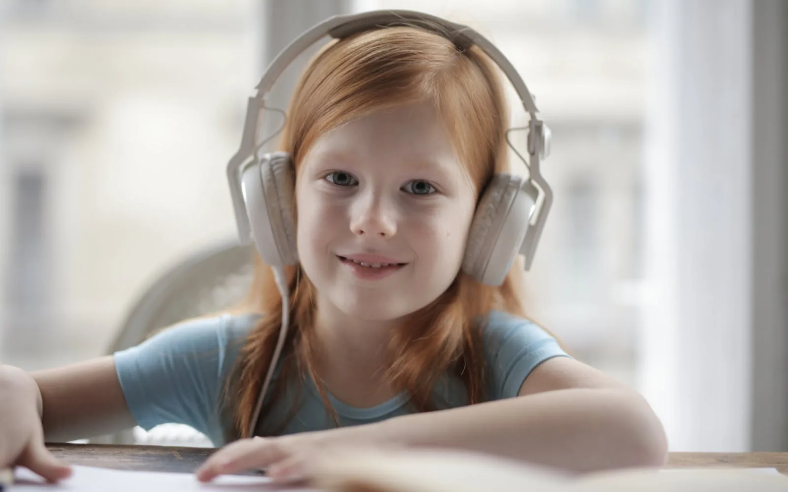 A young girl smiling while listening to music on headphones, enjoying relaxation indoors.
