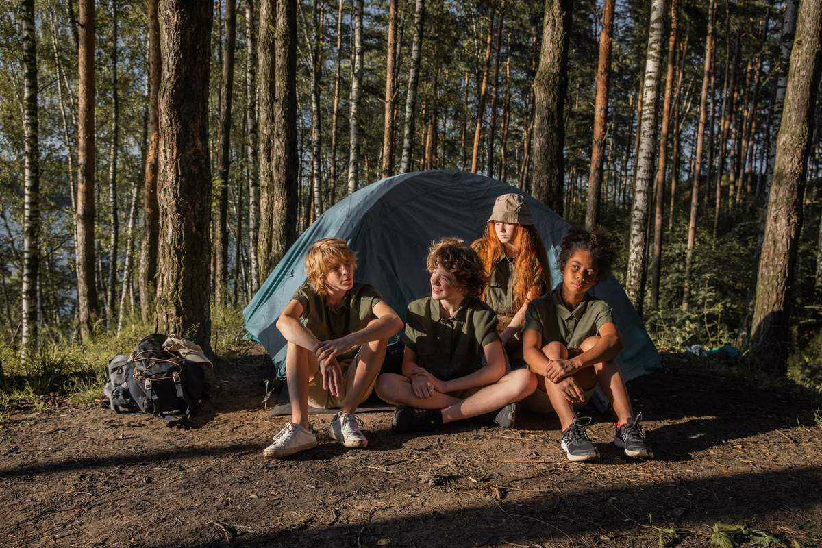 Quatre enfants assis devant une tente verte en colonie de vacances dans la foret