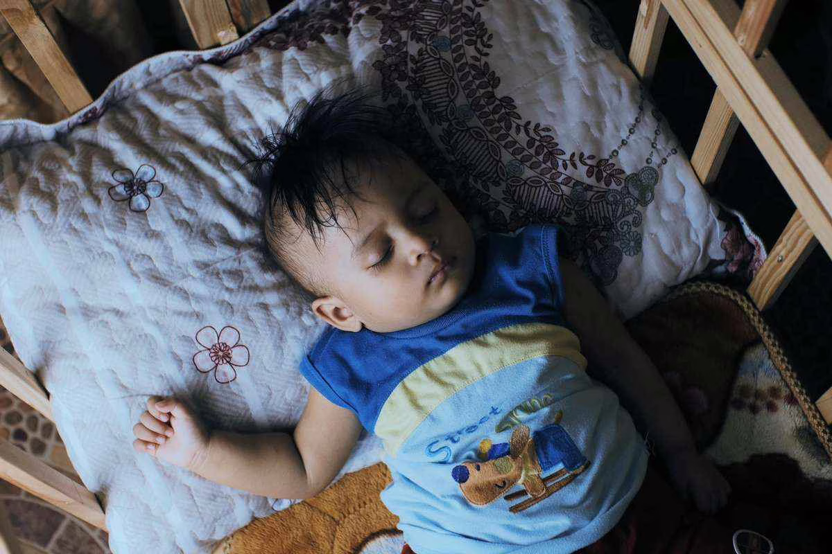 Bébé qui dort paisiblement dans son lit pendant l'été, illustration du ventilateur dans la chambre de bébé en cas de fortes chaleurs