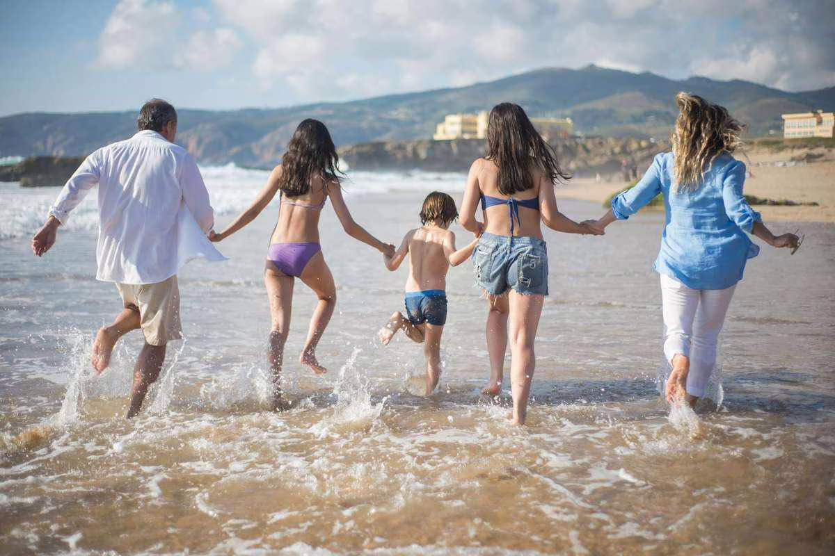 Famille avec enfants qui court vers la mer sur une plage ensoleillée, illustration des aides aux vacances de la Caf pour l'été 2026