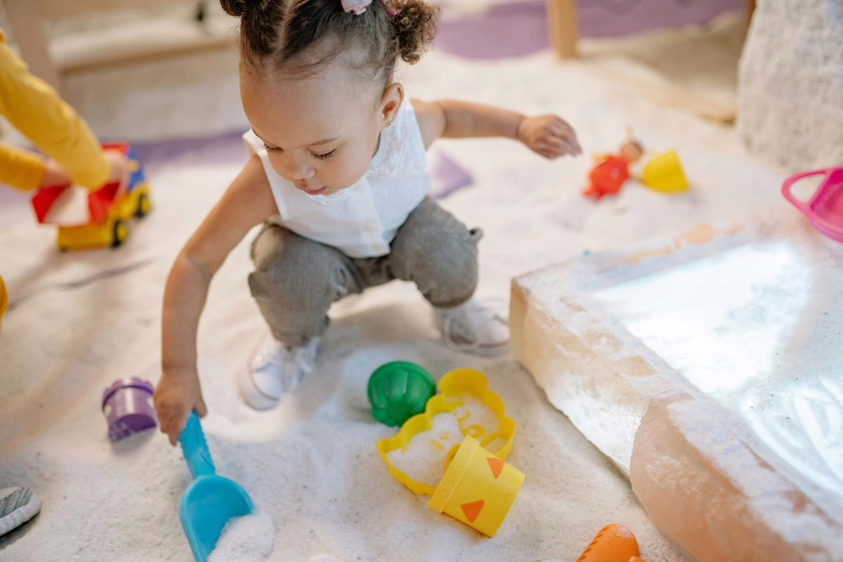 Jeune enfant jouant avec des jouets de sable colorés, illustration du rappel de jeux de sable contenant de l'amiante