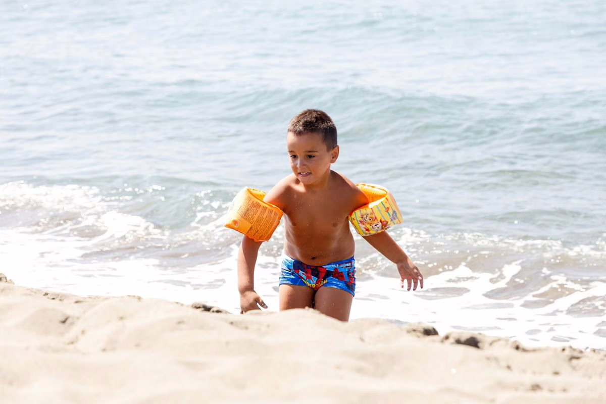 Jeune enfant portant des brassards gonflables dans une piscine, accompagné d'un adulte attentif