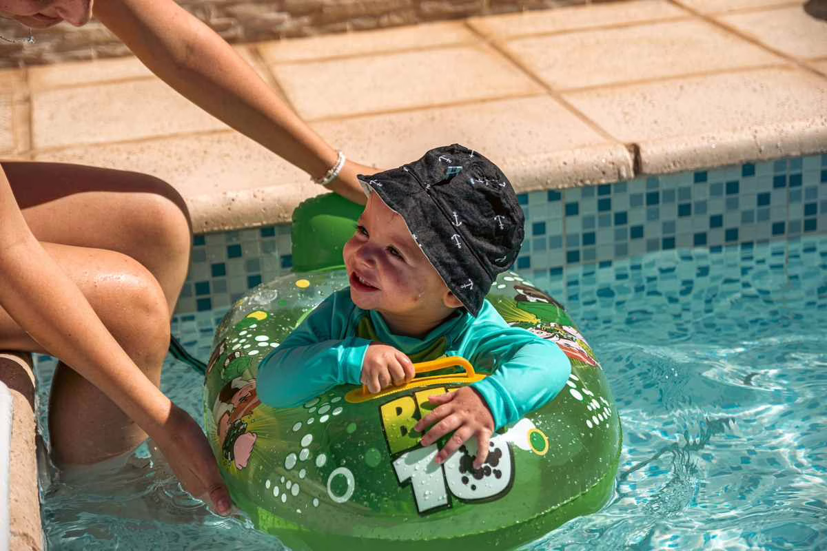 Parent tenant un bebe dans l'eau d'une piscine exterieure par une belle journee d'ete