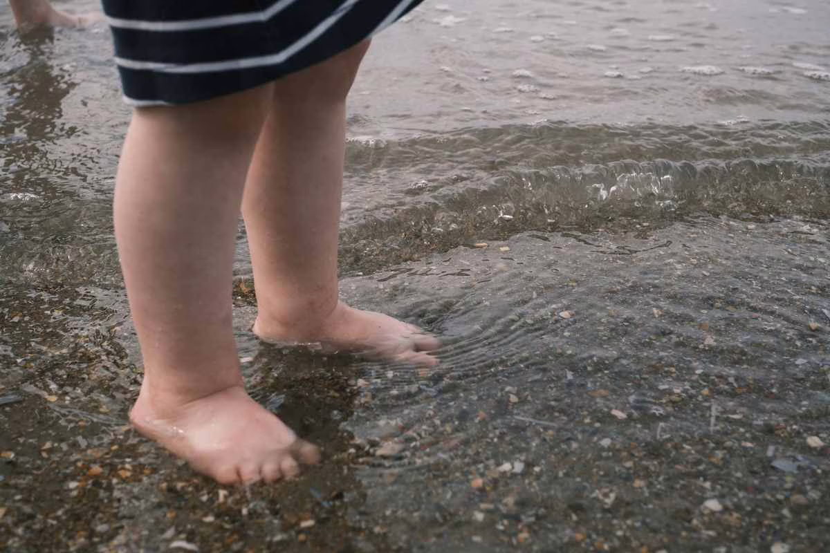 Pieds nus d'un enfant sur le sable mouillé au bord de l'eau, zone où se cache la vive