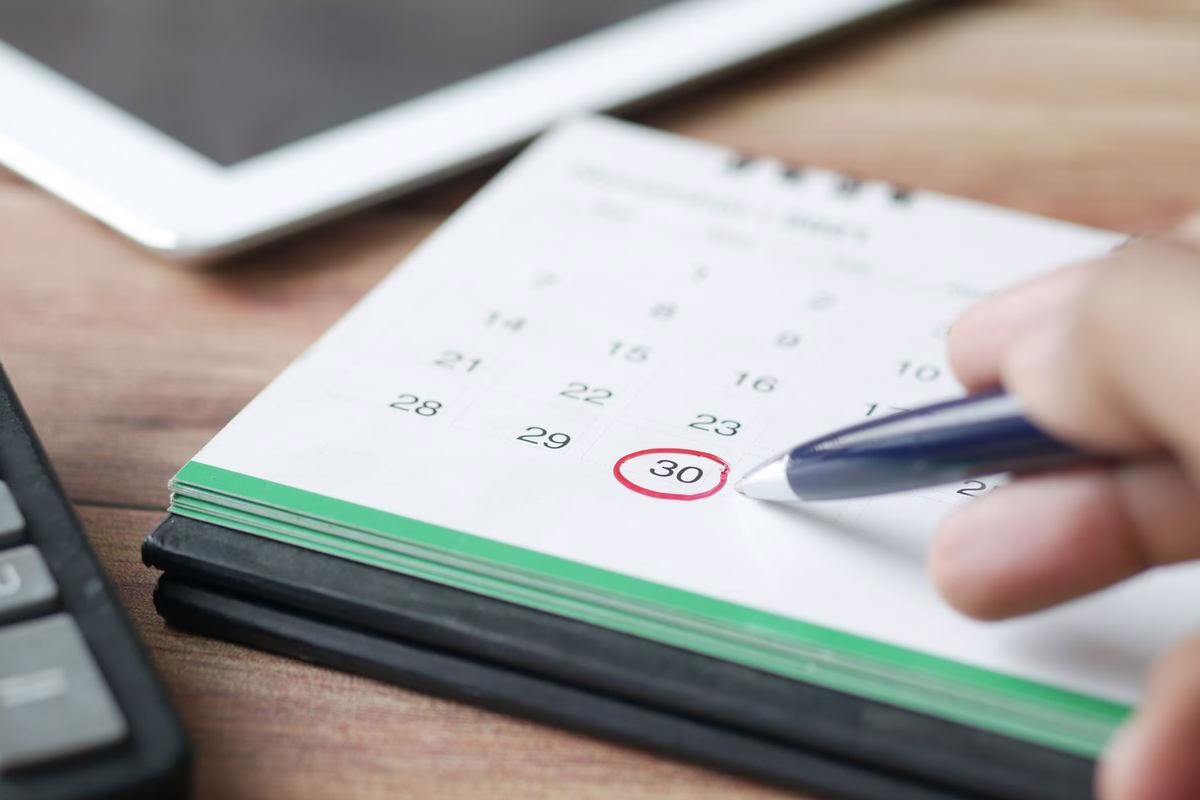 Main entourant une date au stylo sur un calendrier papier posé sur un bureau