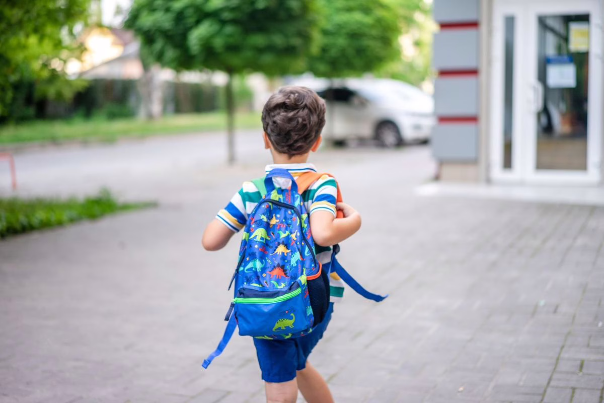 Parent accompagnant son enfant avec cartable devant l'entrée de l'école, un matin de classe
