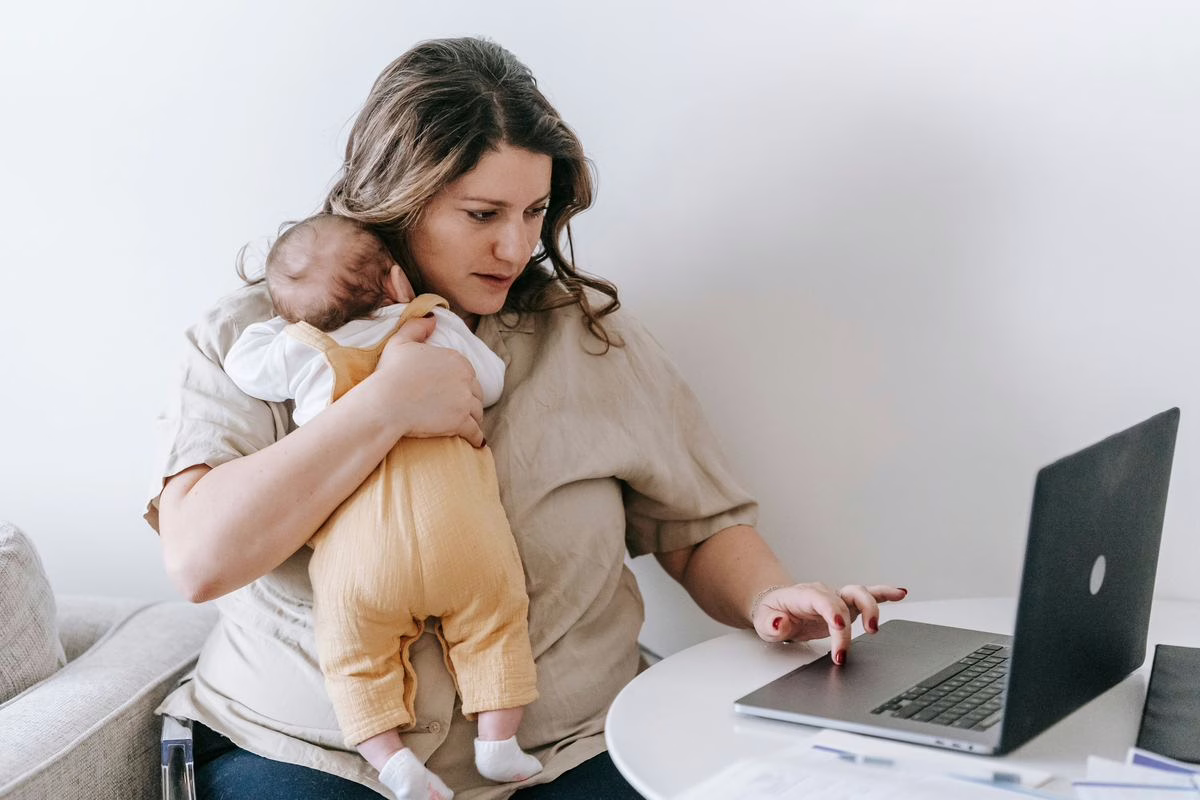 Mere tenant son nouveau-ne devant un ordinateur portable pour suivre le versement du conge de naissance