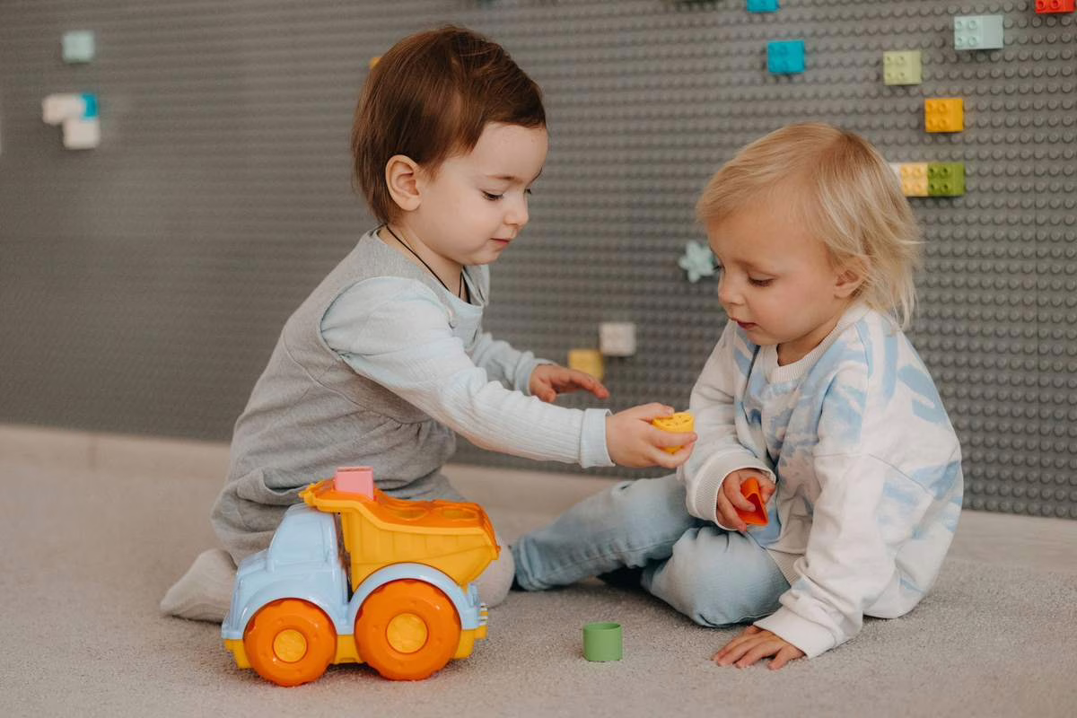 Deux tout-petits jouent avec des jouets en intérieur dans un espace d'accueil collectif, illustration du décret crèche du 1er août 2026