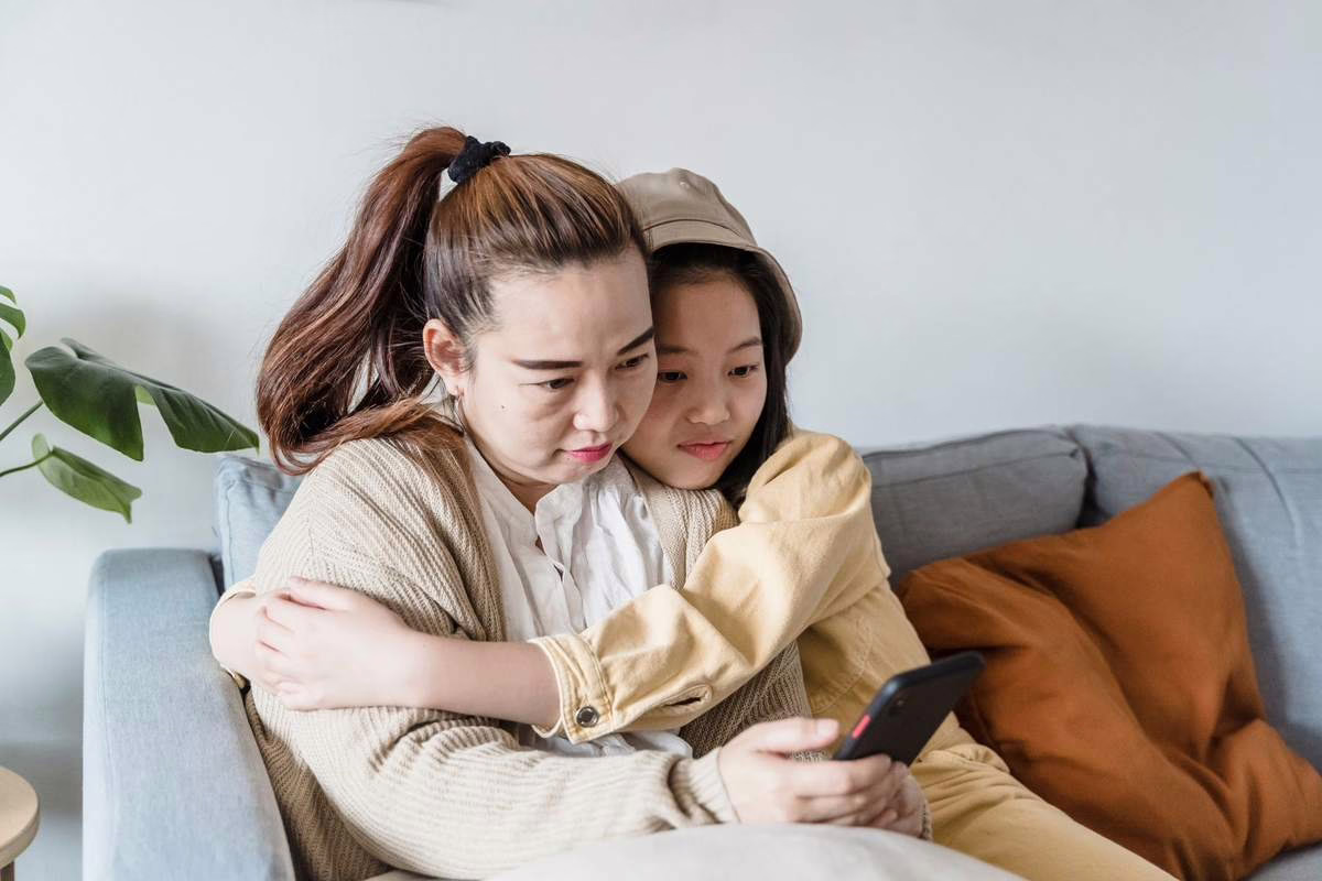 Mère et fille regardant ensemble un smartphone sur le canapé du salon