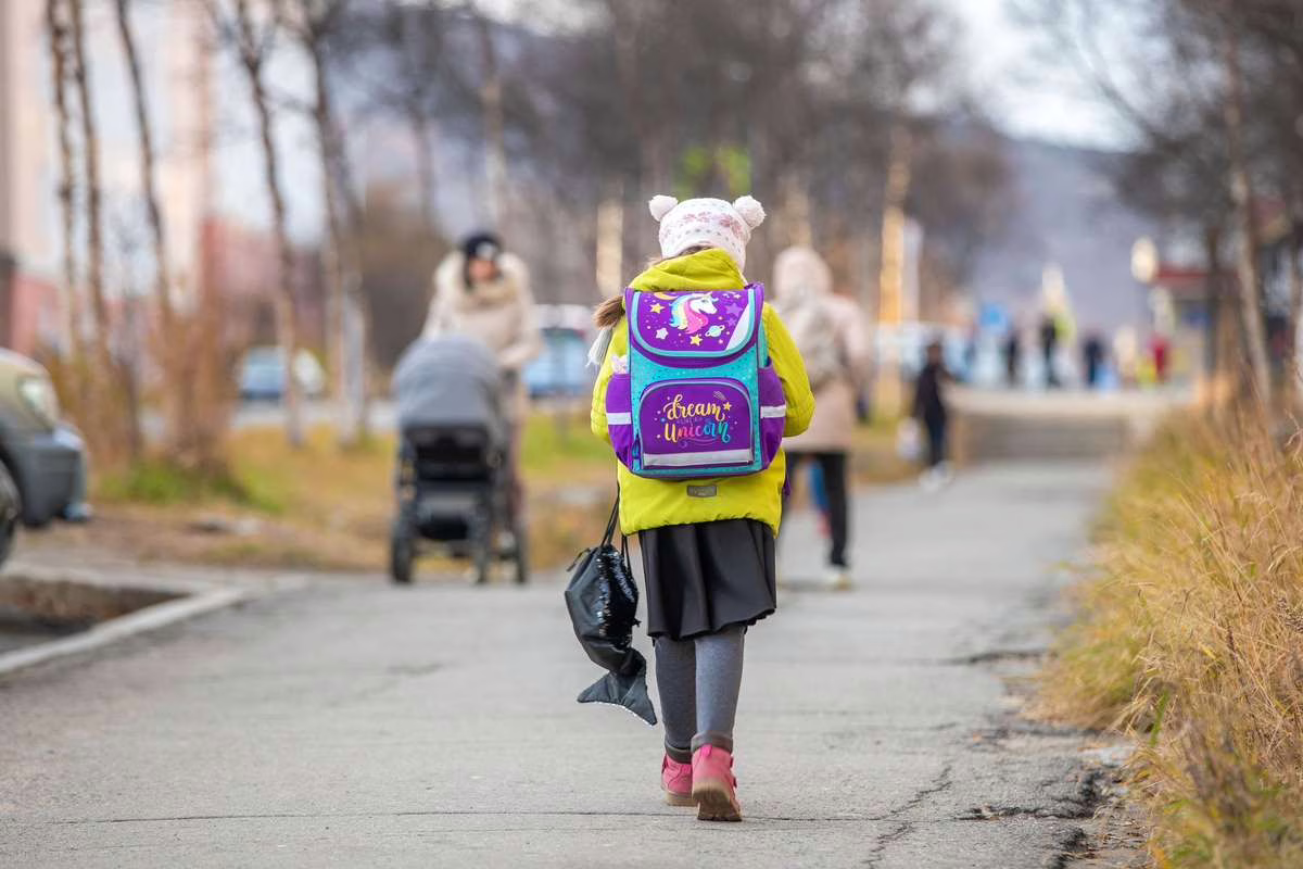 Un écolier porte un cartable visiblement chargé sur les épaules en marchant vers son école