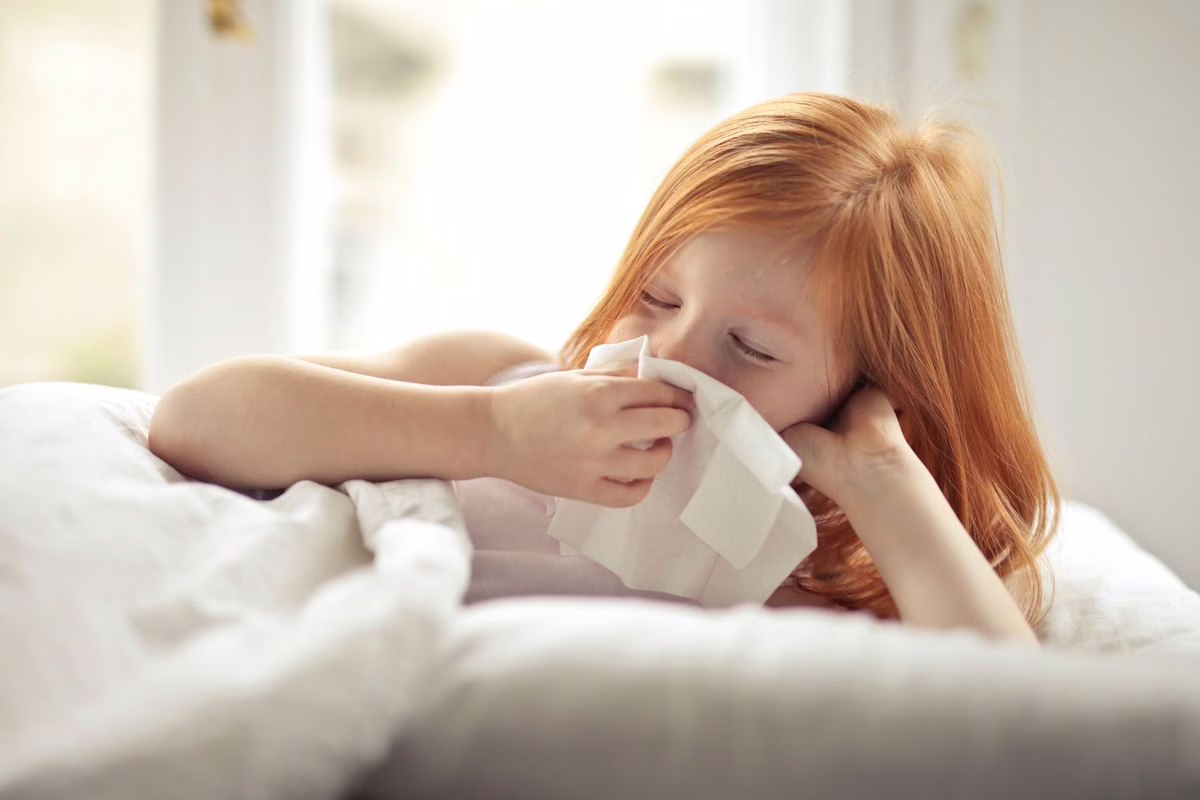 Enfant qui se mouche en plein été dans un jardin, signe possible d'allergie au pollen d'ambroisie