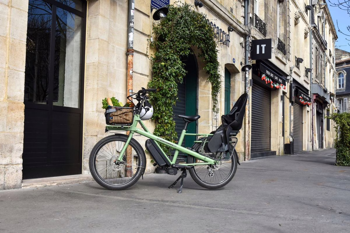 Vélo longtail électrique équipé d'un siège enfant dans une rue française, alternative à la remorque vélo