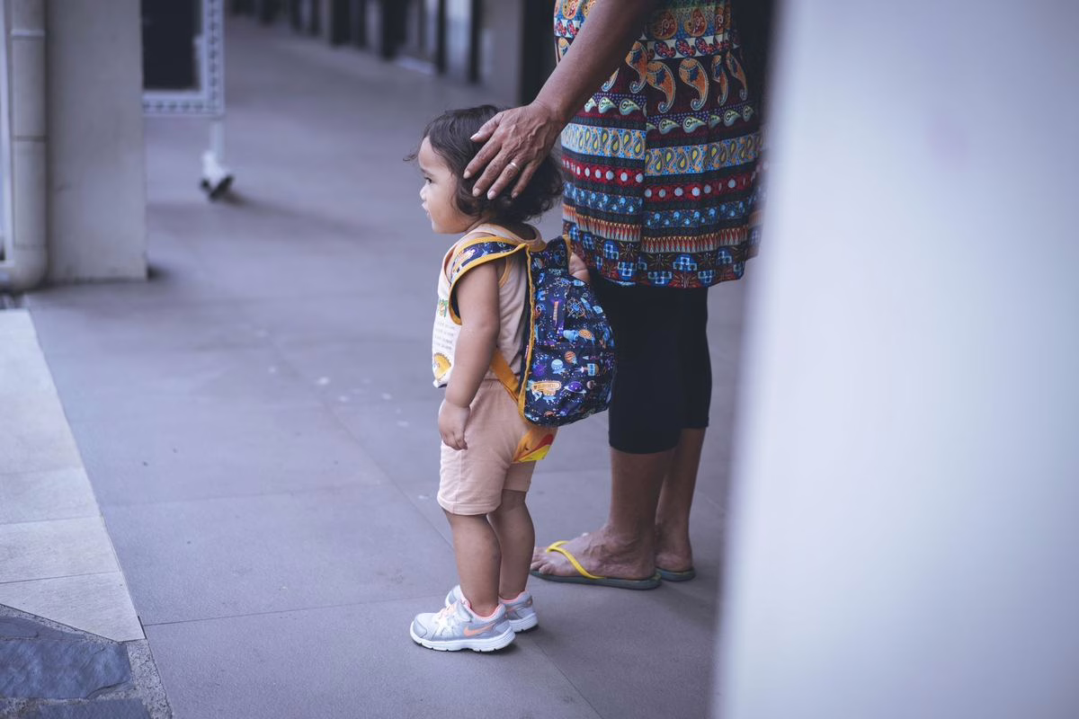 Jeune enfant avec son cartable devant l'école, illustration de la première rentrée en maternelle