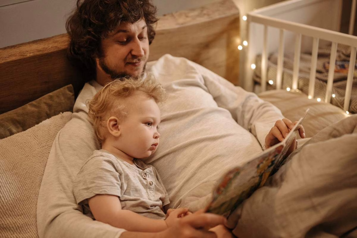 Un adulte lit une histoire à voix haute à un jeune enfant installé contre lui dans le salon