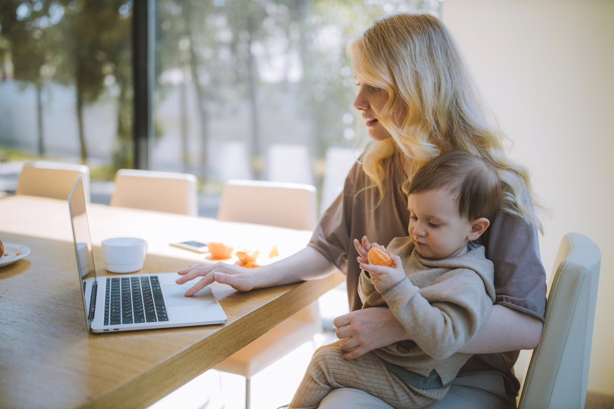 Maman auto-entrepreneur travaillant sur ordinateur portable avec son bébé sur les genoux